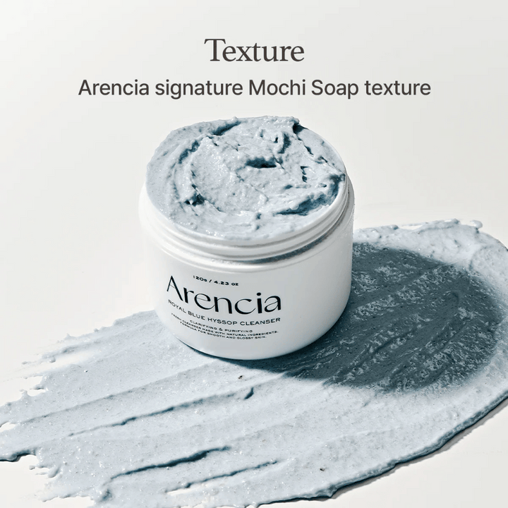 Pot ouvert avec Arencia Fresh Blue Hyssop Rice Mochi Cleanser, placé sur une couche étalée de la formule nettoyante bleue et crémeuse qui montre sa texture semblable à du mochi.