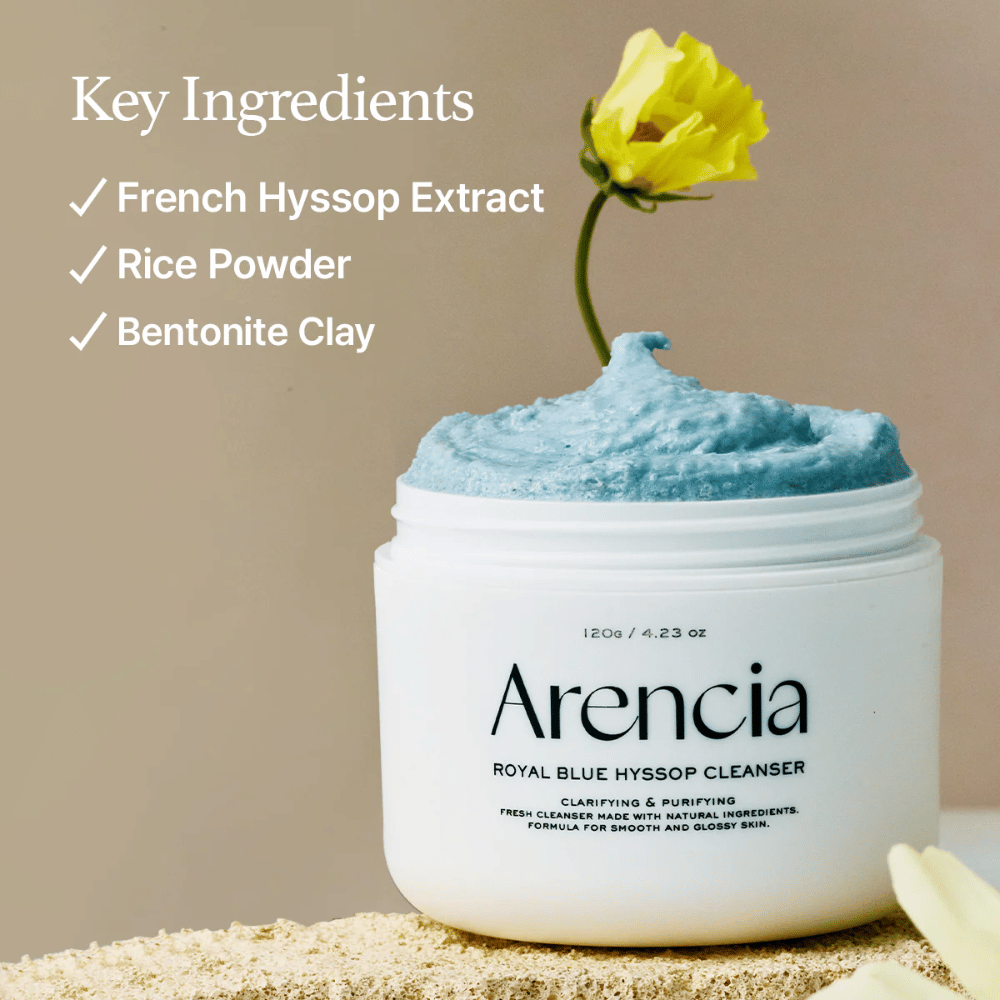 Image du pot "Arencia Royal Blue Hyssop Cleanser" rempli de crème nettoyante bleue. Une fleur jaune dépasse de la crème. Le texte de l'image met en avant trois ingrédients clés : extrait d'hysope française, poudre de riz et argile bentonite.