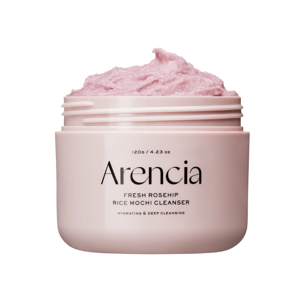 Gros plan sur un pot rose avec Arencia Royal Rosehip Cleanser, rempli de crème nettoyante rose avec une texture fouettée semblable à celle du mochi. Le texte sur le pot indique que le produit hydrate et nettoie en profondeur.