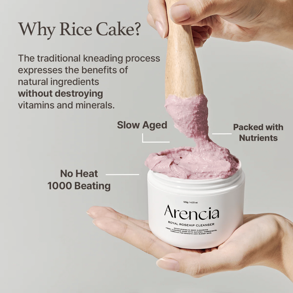 Une main tient un pot ouvert de Arencia Royal Rosehip Cleanser, avec une formule nettoyante rose semblable à celle du mochi soulevée avec une spatule en bois - montrant la texture du produit et la méthode de fabrication traditionnelle.