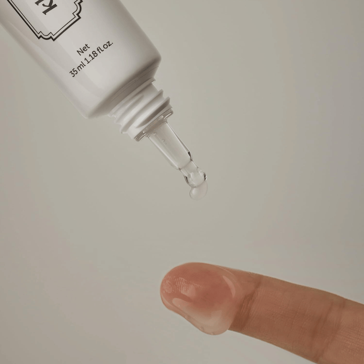 Image en gros plan où un gel clair et léger est appliqué depuis l’embout fin sur un doigt. L’image illustre la texture transparente à base de gel du produit ainsi que l’application précise autour du contour des yeux.