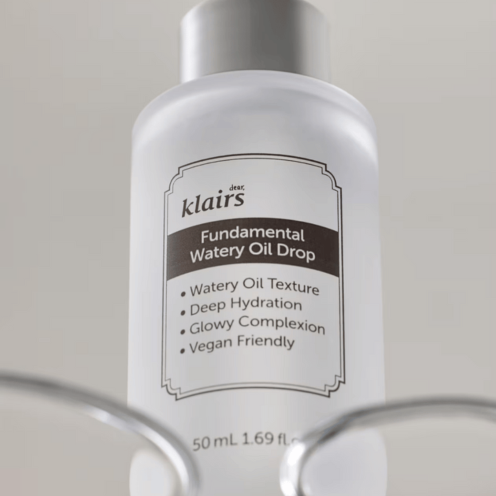 Flacon avec Klairs Fundamental Watery Oil Drop, 50 ml, placé dans un support transparent, avec une étiquette claire mettant en avant les propriétés hydratantes et véganes du produit.