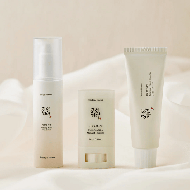 Trois produits solaires de Beauty of Joseon – Ginseng Moist Sun Serum, Matte Sun Stick et Relief Sun Rice + Probiotics – alignés sur un tissu couleur crème avec une lumière douce.