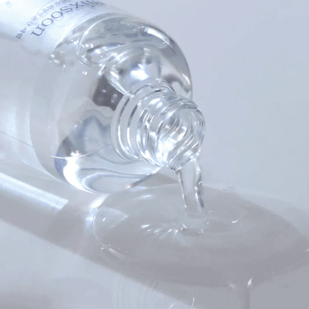 Gros plan sur un sérum transparent versé d'une bouteille Mixsoon Glacier Water Hyaluronic Acid Serum sur une surface brillante.