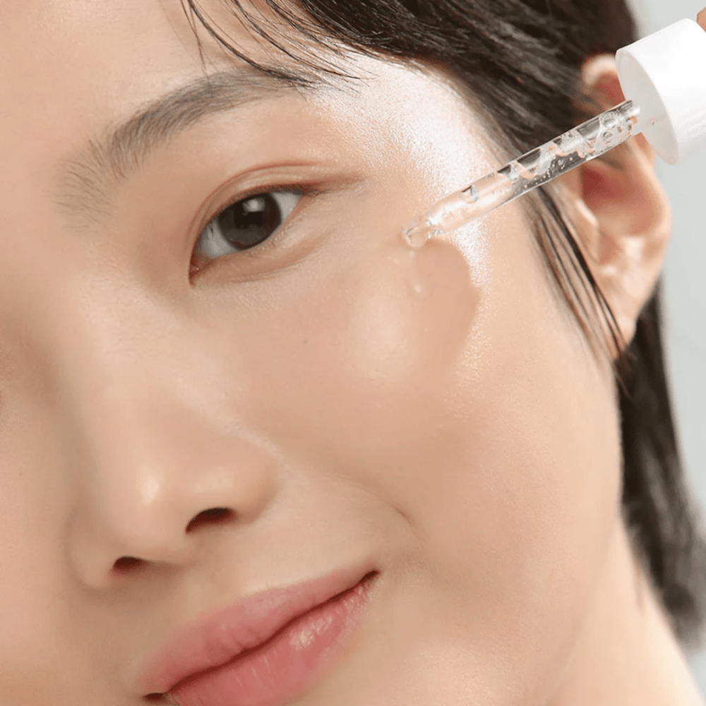 Gros plan sur une femme appliquant du sérum sur la joue avec une pipette – soins de la peau qui donnent de l'éclat et de l'hydratation.