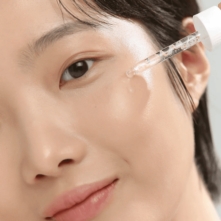 Gros plan sur une femme appliquant du sérum sur la joue avec une pipette – soins de la peau qui donnent de l'éclat et de l'hydratation.