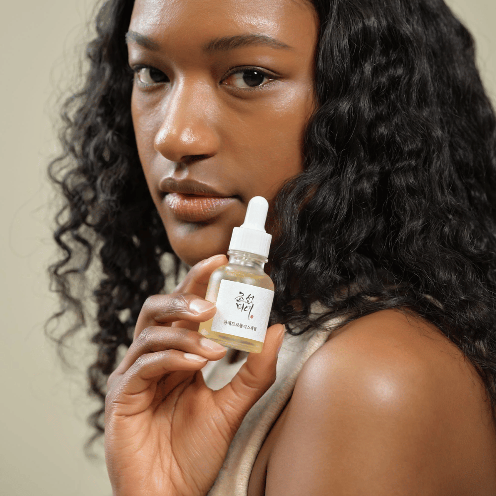 Femme aux cheveux bouclés tenant un flacon de Beauty of Joseon Glow Serum avec pipette, un produit de soin hydratant et illuminant.