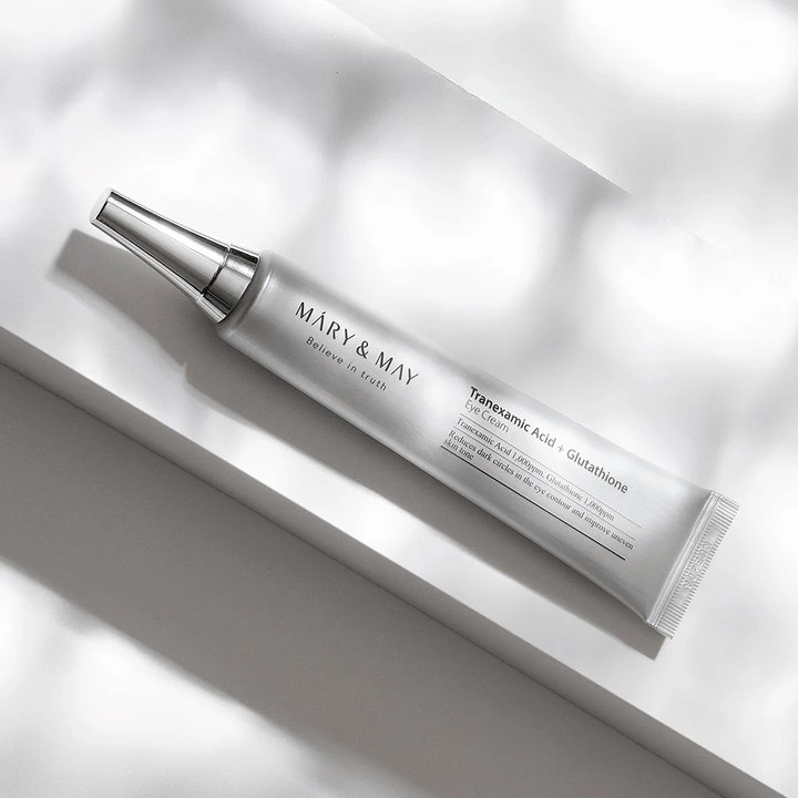 Gros plan de Mary&May Tranexamic Acid + Glutathione Eye Cream avec applicateur métallique, développé pour éclaircir les cernes et unifier le teint autour des yeux.
