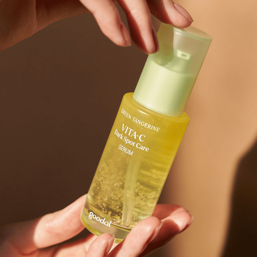Une personne tenant une bouteille Green Tangerine Vita C Dark Spot Care Serum 40ml de Goodal pour l'hyperpigmentation et le soin des taches sombres.