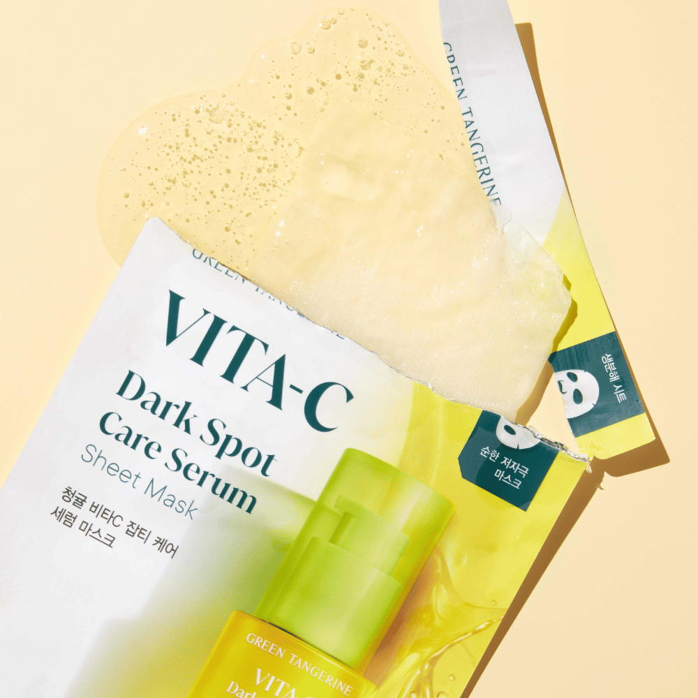 Emballage ouvert de VITA-C Dark Spot Care Serum Masque tissu avec un masque facial dessus et une bouteille de sérum verte, le tout sur un fond jaune.