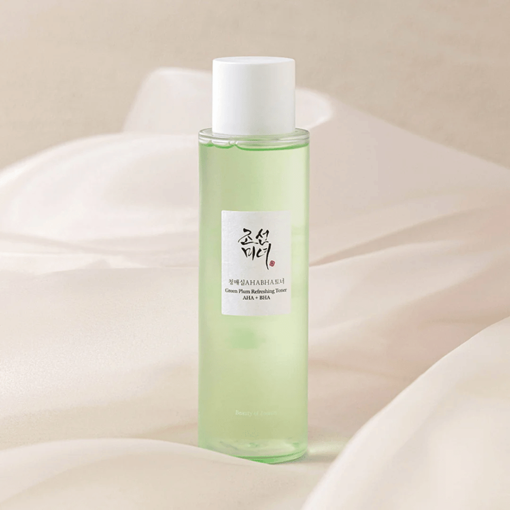 Une bouteille de "Green Plum Refreshing Toner" AHA + BHA se tient sur un fond doux et clair. Le produit a un liquide vert qui reflète la fraîcheur et la naturalité. L'étiquette est blanche avec des touches noires et rouges, ce qui donne un look élégant et pur.