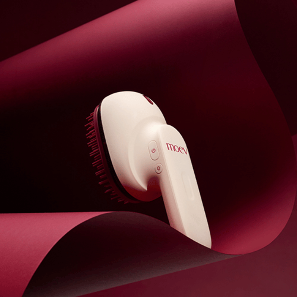 MOEV Hair Steamer Pro dans un design élégant sur fond rouge. Brosse de soin des cheveux innovante qui utilise la vapeur et la chaleur pour apporter brillance, douceur et santé capillaire renforcée.