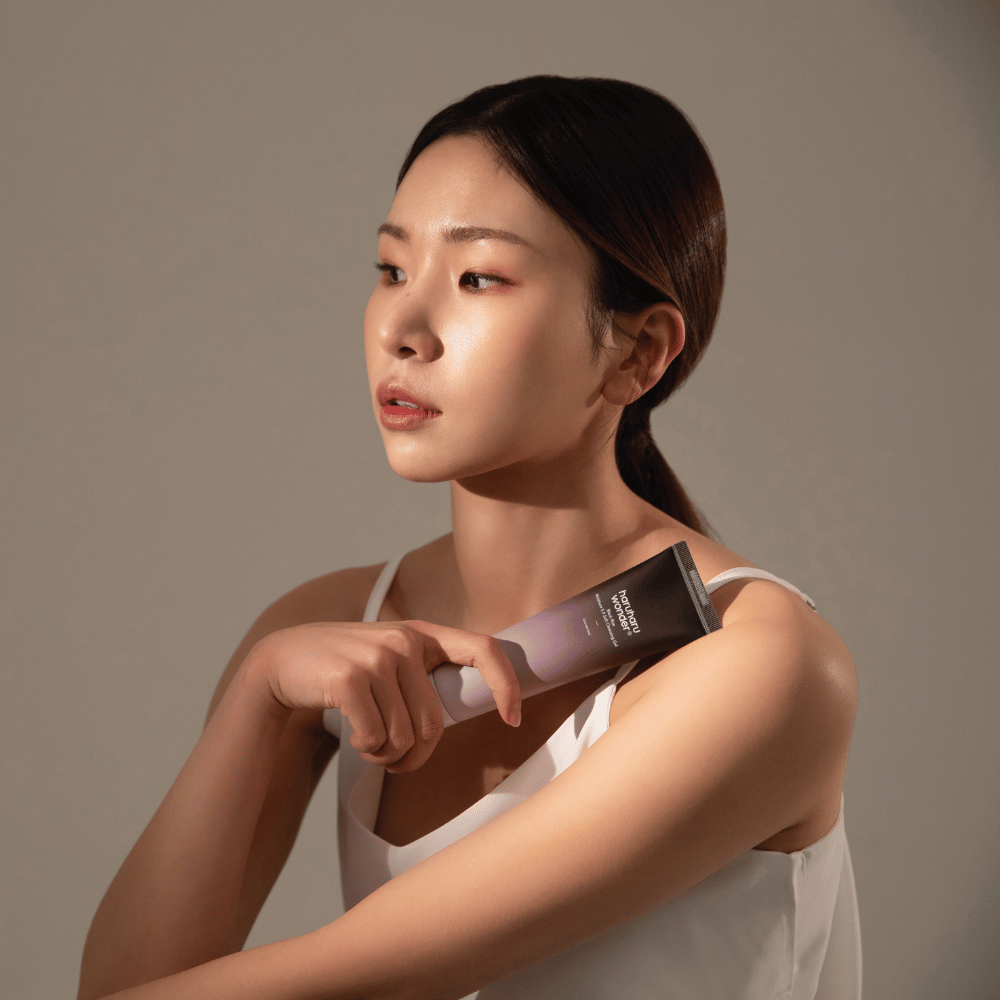 Une jeune femme asiatique tenant une brosse à la main tout en utilisant Haruharu Wonders Black Rice Moisture 5.5 Soft Cleansing Gel 100ml.