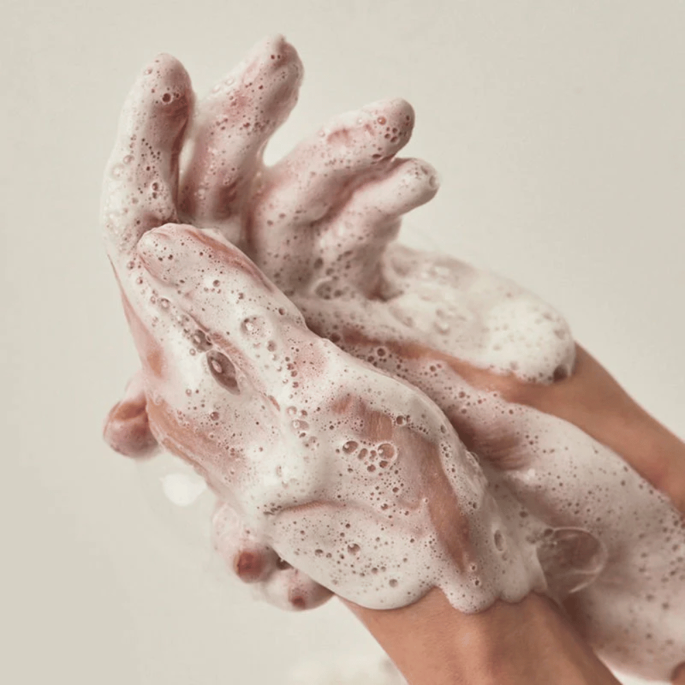 Gros plan sur des mains couvertes d’une mousse nettoyante riche et crémeuse. L’image illustre la mousse et les propriétés nettoyantes du produit tout en donnant une sensation claire d’utilisation et de texture.