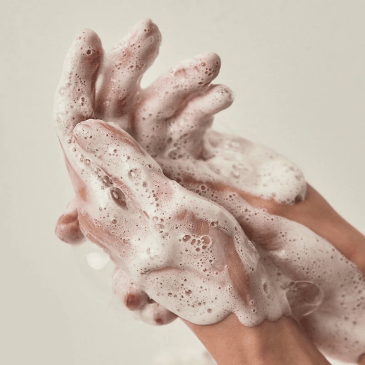 Gros plan sur des mains couvertes d’une mousse nettoyante riche et crémeuse. L’image illustre la mousse et les propriétés nettoyantes du produit tout en donnant une sensation claire d’utilisation et de texture.