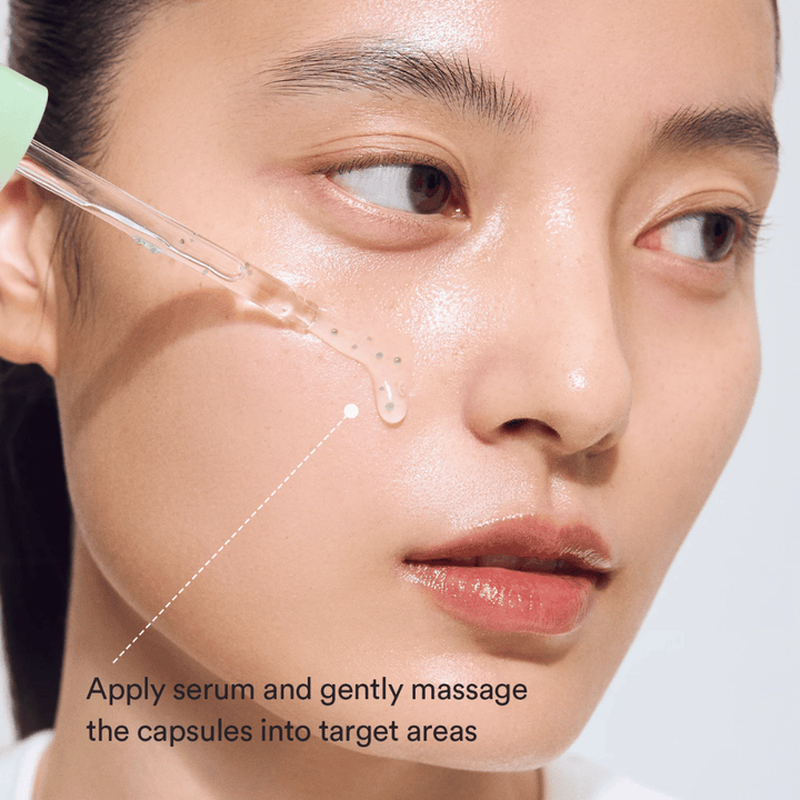 Gros plan d’un modèle appliquant le sérum avec une pipette pendant que les capsules vertes sont massées dans la peau pour un effet apaisant et hydratant.