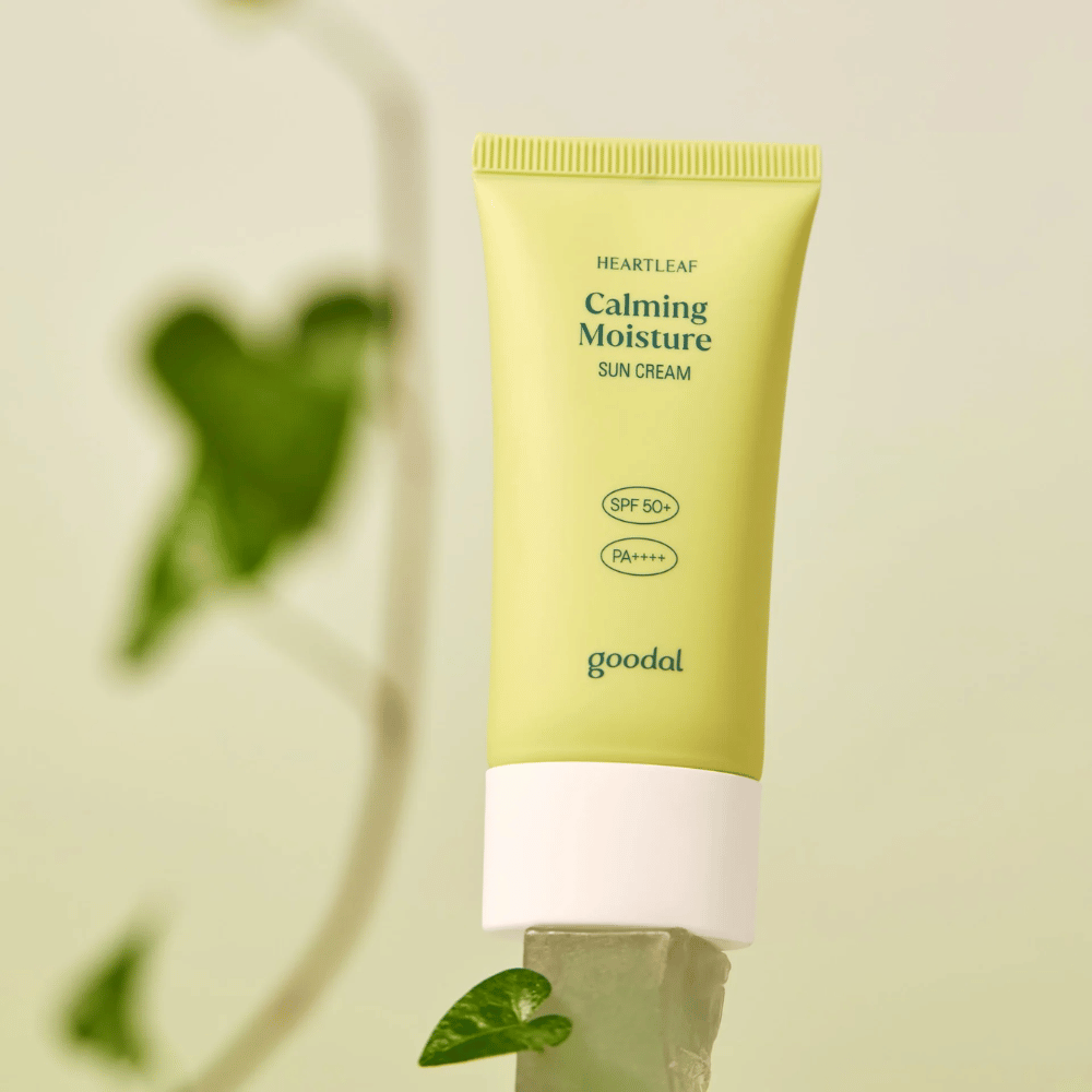Goodal Heartleaf Calming Moisture Sun Cream SPF50+ PA++++ placé sur une plaque de verre avec une plante verte en arrière-plan - une crème solaire apaisante pour la peau sensible.
