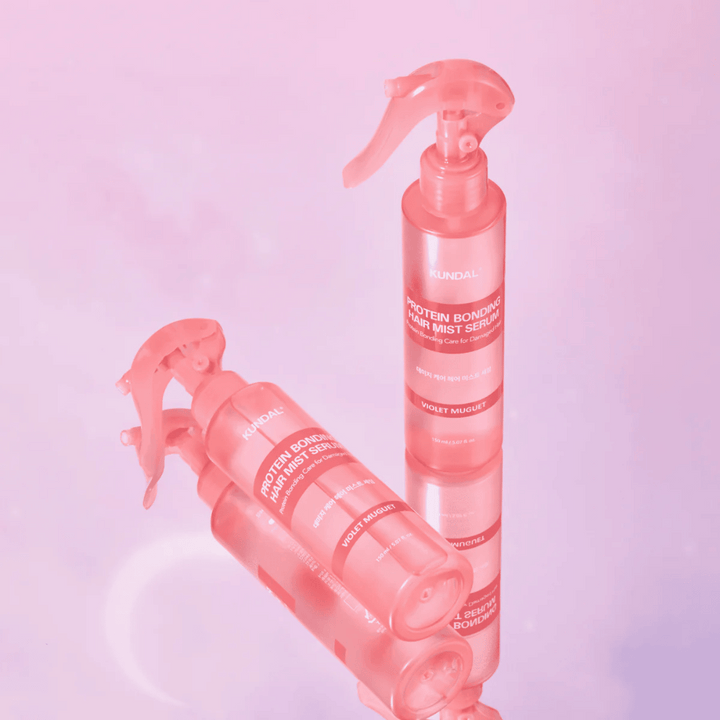 KUNDAL Sérum Brume Cheveux à Liaison Protéique Violet Muguet dans des flacons pulvérisateurs roses, debout et couché sur un fond rose clair avec réflexion.