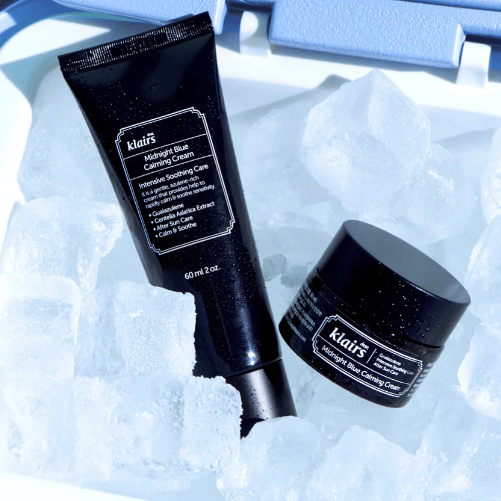 Un tube et un pot de Klairs Midnight Blue Calming Cream reposent sur des glaçons, mettant l'accent sur les propriétés apaisantes et hydratantes, sur un fond bleu.
