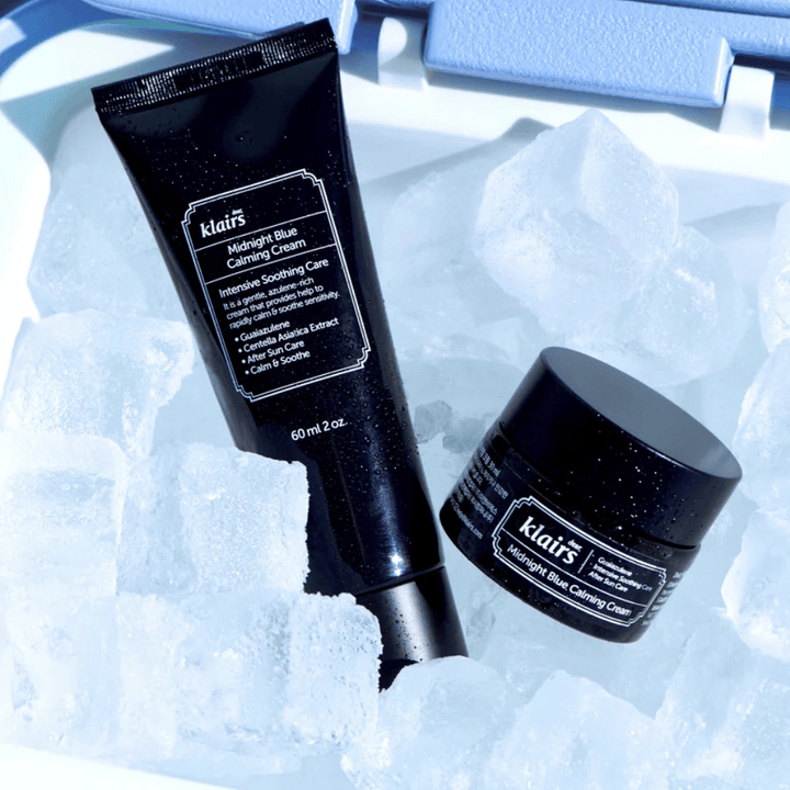 Un tube et un pot de Klairs Midnight Blue Calming Cream reposent sur des glaçons, mettant l'accent sur les propriétés apaisantes et hydratantes, sur un fond bleu.