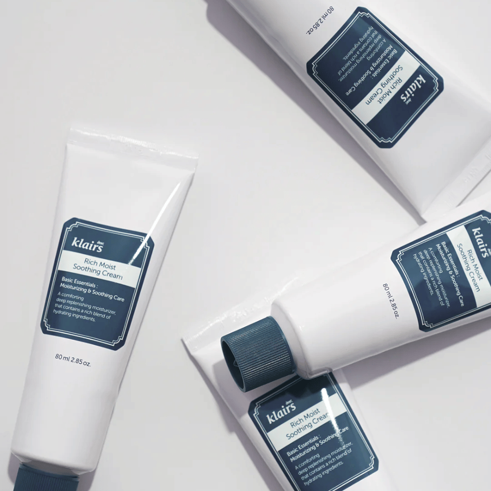 Plusieurs tubes de Klairs Rich Moist Soothing Cream stratégiquement placés sur une surface claire, avec des ombres créant de la profondeur.