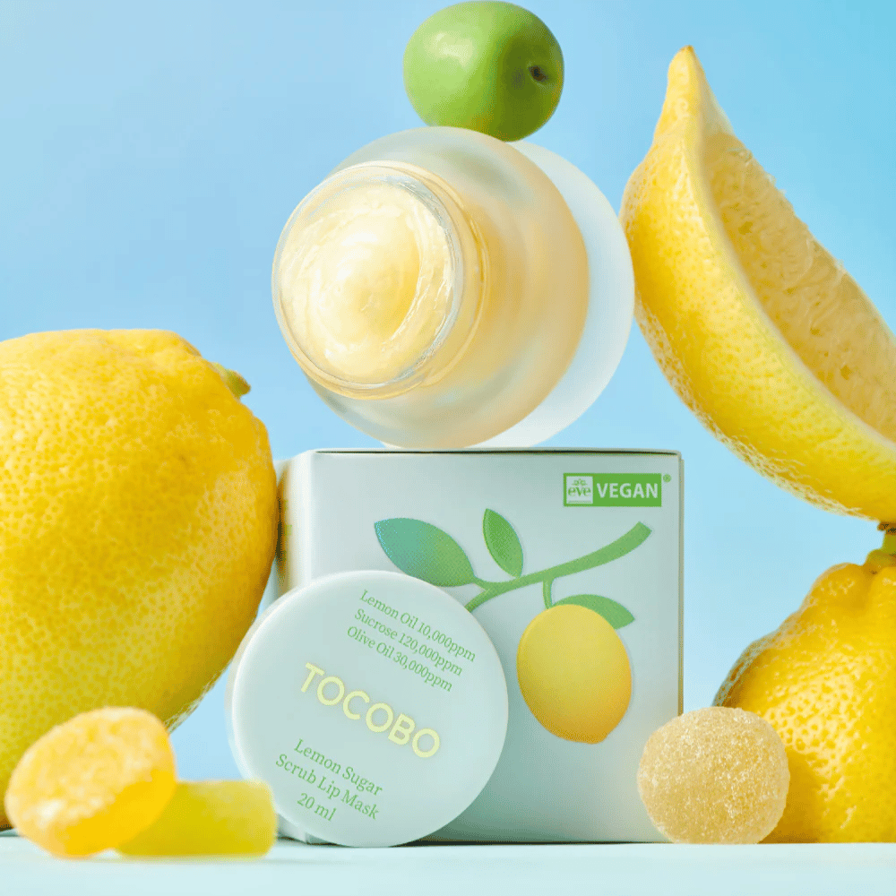 Pot avec Tocobo Lemon Sugar Scrub Lip Mask placé parmi des citrons et l'emballage, marqué comme végétalien.