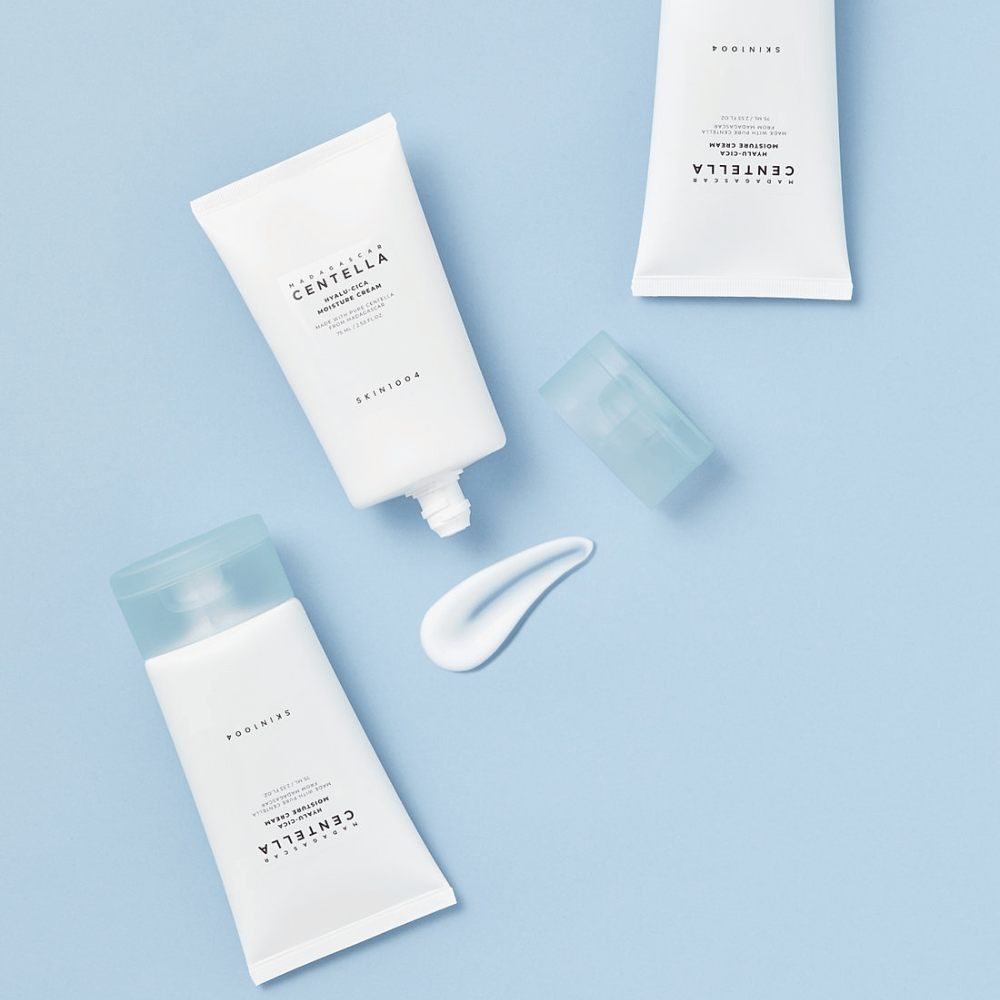 Deux tubes blancs avec SKIN1004 produits de soin de la peau Centella, une noisette de produit et un bouchon bleu clair, sur un fond bleu clair.