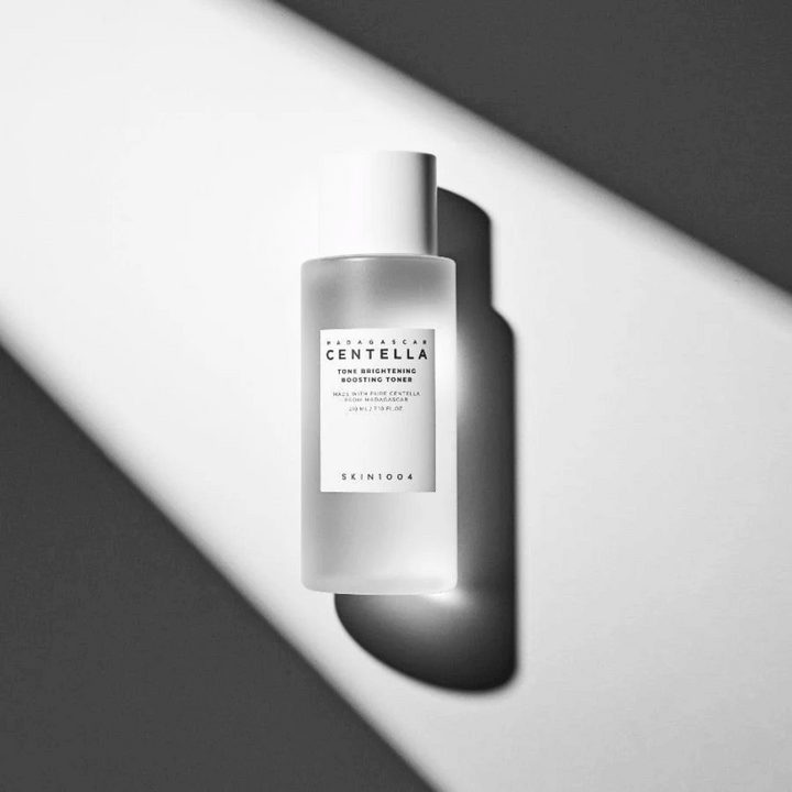Bouteille de SKIN1004 Madagascar Centella Tone Brightening Boosting Toner  couchée sur une surface blanche avec une ombre dramatique dans un jeu de lumière noir et blanc.