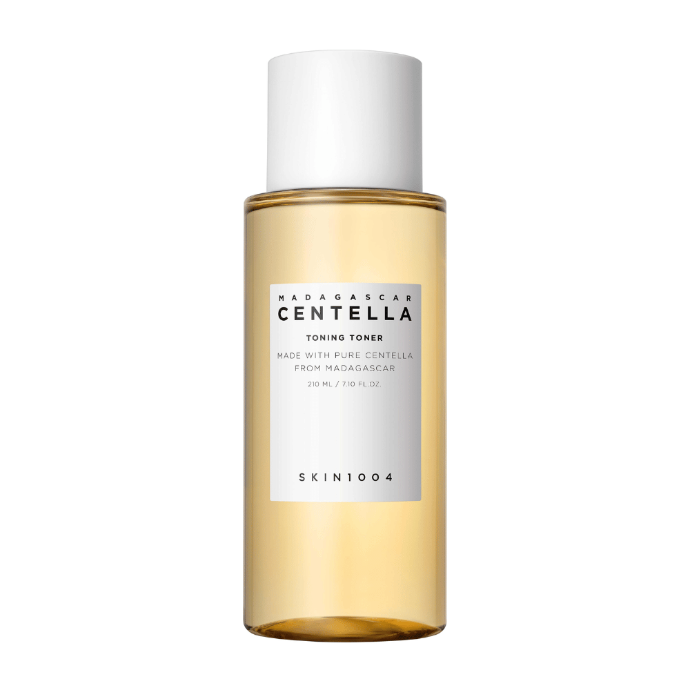 L'image montre une bouteille de tonique pour la peau, étiquetée "Madagascar Centella Toning Toner" de SKIN1004. Le produit est indiqué comme contenant 210 ml ou 7,10 fl.oz et est fabriqué avec de la Centella pure de Madagascar. L'emballage est simple et élégant avec une bouteille transparente et un liquide doré à l'intérieur, ce qui donne une impression de luxe et de pureté. Le logo de la marque SKIN1004 est clairement visible dans la partie inférieure de l'étiquette.