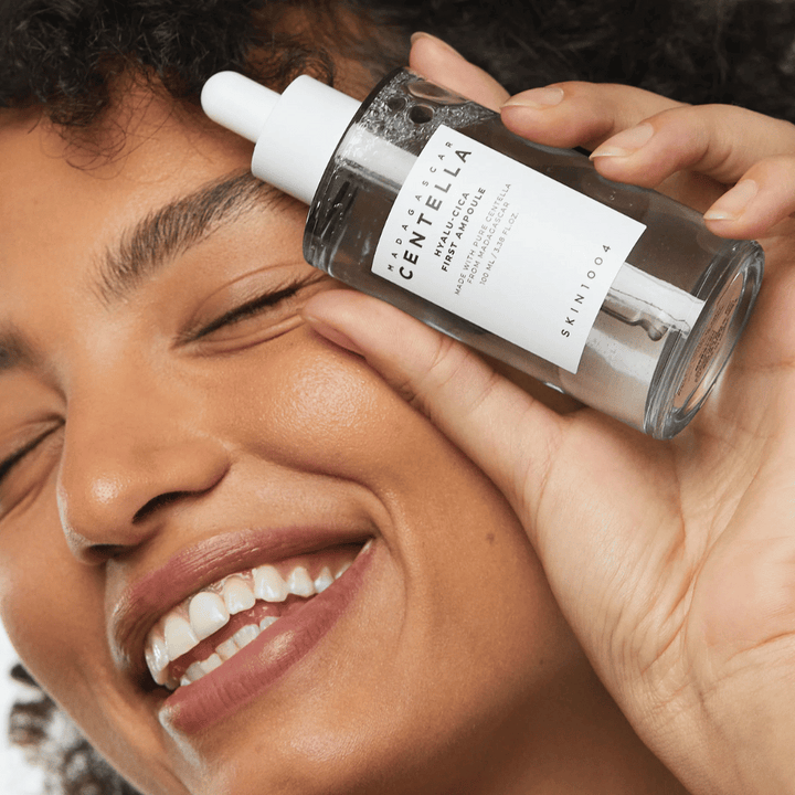 Femme souriante tenant Skin1004 Madagascar Centella Hyalu-Cica First Ampoule à côté du visage.