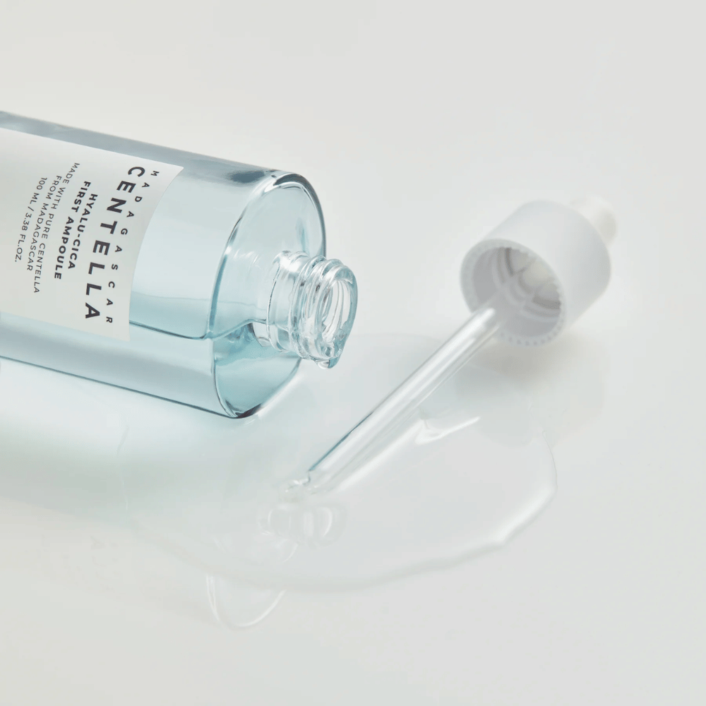 Gros plan sur flacon ouvert Skin1004 Madagascar Centella Hyalu-Cica First Ampoule avec pipette posée et sérum répandu sur surface blanche.