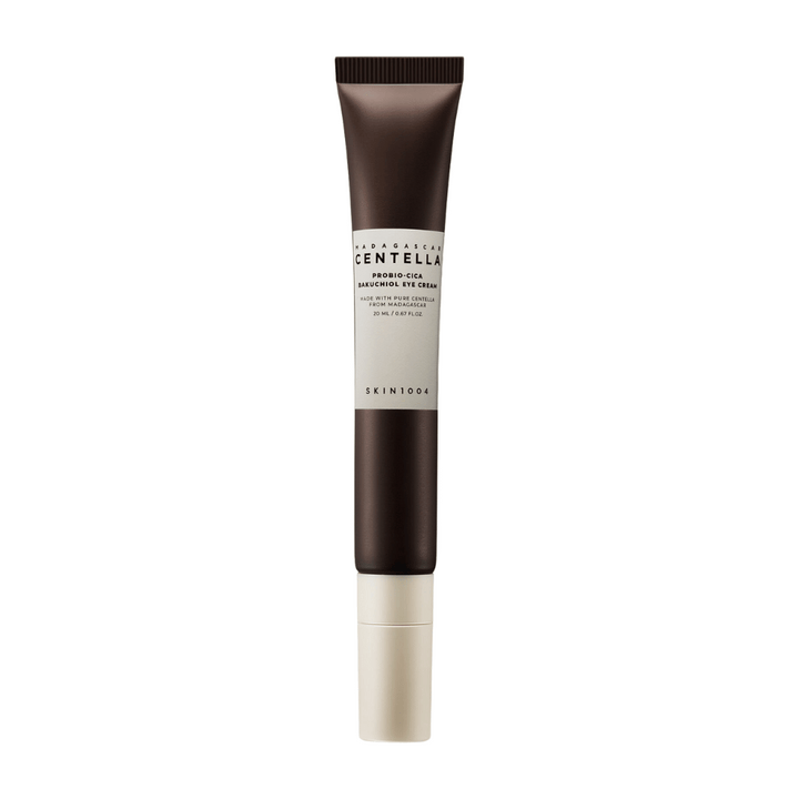 Un tube de "Madagascar Centella Probio-Cica Bakuchiol Eye Cream" de SKIN1004. Le produit est conçu pour la zone des yeux et contient des ingrédients tels que la centella de Madagascar et le bakuchiol, connus pour leurs propriétés de soin de la peau et d'hydratation. Le tube est élégant avec une couleur brun foncé passant au blanc.