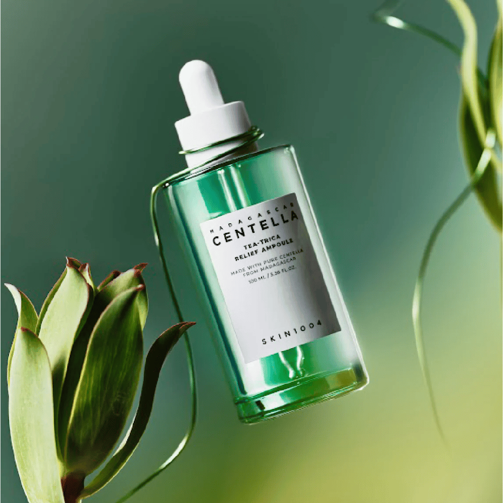 SKIN1004 Madagascar Centella Tea-Trica Relief Ampoule – bouteille en verre vert avec pipette, étiquette blanche et contenu de 100 ml, photographiée sur fond vert avec des détails de plantes.