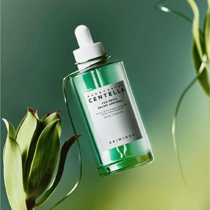 SKIN1004 Madagascar Centella Tea-Trica Relief Ampoule – bouteille en verre vert avec pipette, étiquette blanche et contenu de 100 ml, photographiée sur fond vert avec des détails de plantes.