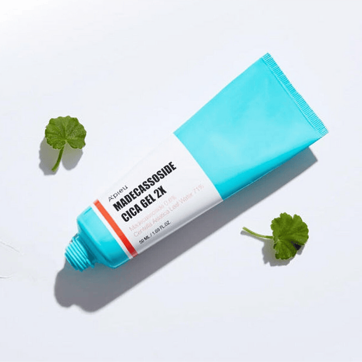 A’pieu Madecassoside Cica Gel 2X en tube bleu avec étiquette blanche, entouré de trois feuilles de centella asiatica vertes sur fond blanc.