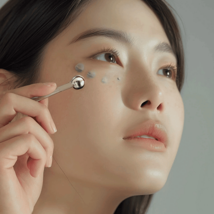 Une femme applique Heimish Marine Care Algae + Peptide Eye Cream sous l'œil avec un applicateur en métal pour un effet rafraîchissant et vivifiant. La crème aide à hydrater et à réduire les signes de l'âge autour des yeux.