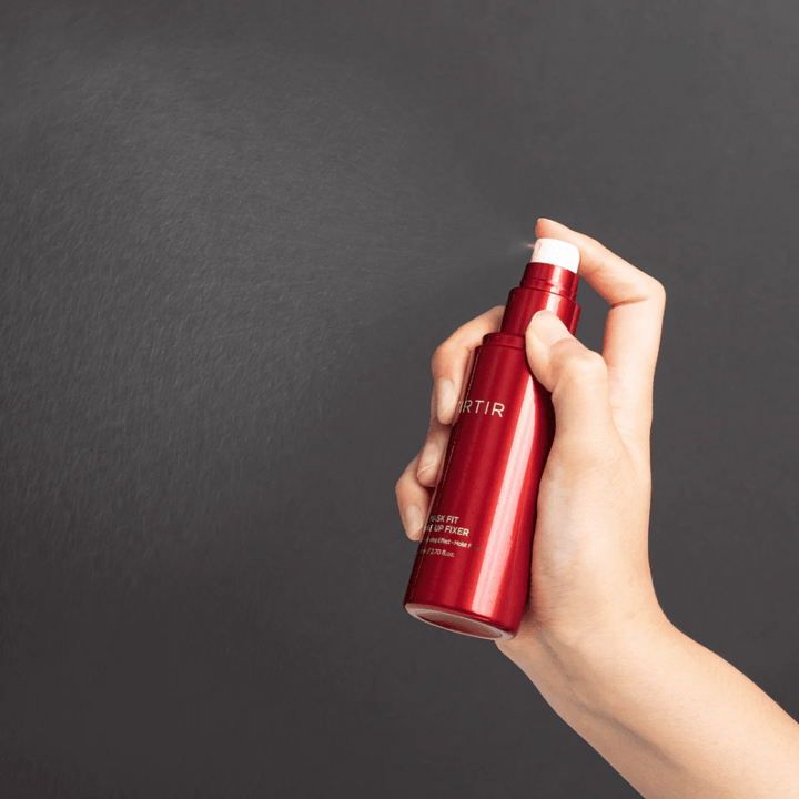 Une main tenant une bouteille rouge de la marque tirtir Mask Fit Make Up Fixer et vaporisant une fine brume, idéale pour fixer le maquillage.
