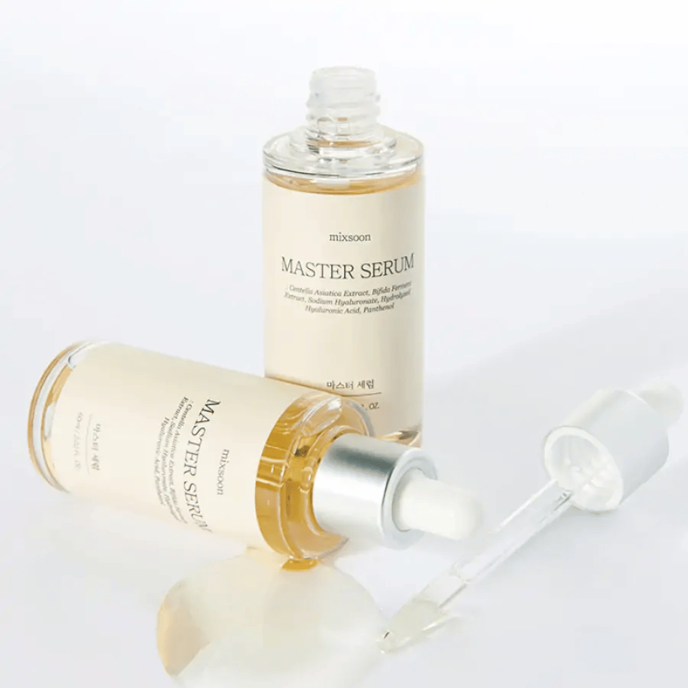 Deux bouteilles Mixsoon Master Serum, une debout et une couchée avec une pipette ouverte, où le sérum s'est répandu sur une surface blanche.