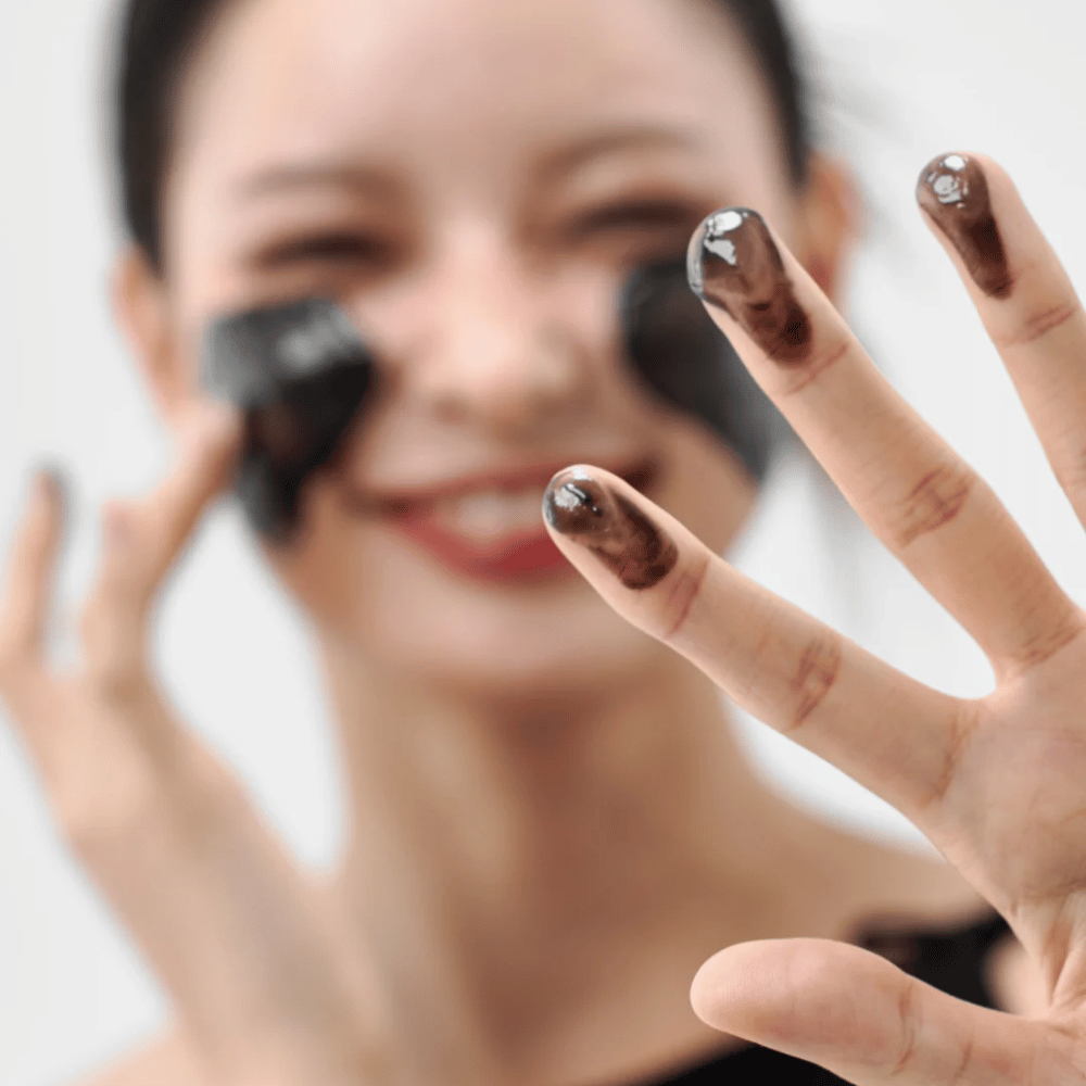 Modèle appliquant Comment Midnight Soothing Cleansing Balm sur la peau. Baume nettoyant crémeux qui nettoie en profondeur et laisse la peau douce et équilibrée.