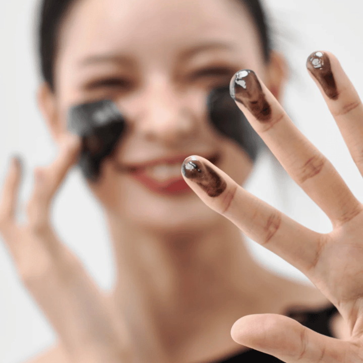 Modèle appliquant Comment Midnight Soothing Cleansing Balm sur la peau. Baume nettoyant crémeux qui nettoie en profondeur et laisse la peau douce et équilibrée.