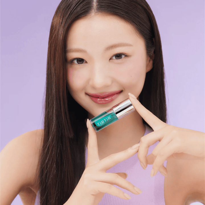 Femme aux cheveux longs et raides tenant un TIRTIR My Glow Lip Oil et montrant ses lèvres roses brillantes sur un fond violet.