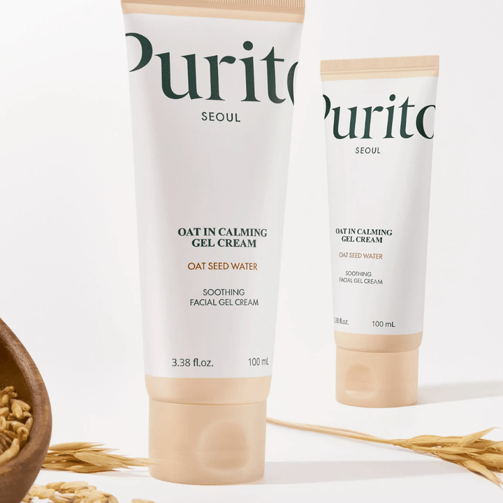 Purito Oat-In Calming Gel Cream dans un tube beige, placé avec des grains d'avoine. Apaise la peau sensible avec de l'eau d'avoine et une texture gel légère.