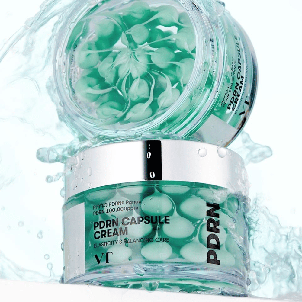 Deux pots de VT PDRN Capsule Cream empilés avec des éclaboussures d'eau autour. Les pots transparents montrent des capsules vertes à l'intérieur, avec le texte "Elasticity & Balancing Care" visible sur l'étiquette.
