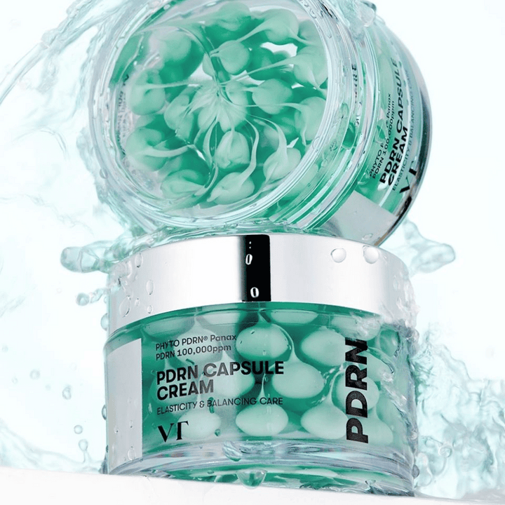 Deux pots de VT PDRN Capsule Cream empilés avec des éclaboussures d'eau autour. Les pots transparents montrent des capsules vertes à l'intérieur, avec le texte "Elasticity & Balancing Care" visible sur l'étiquette.