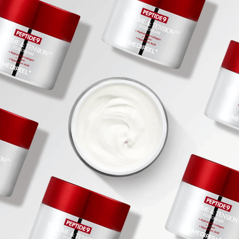 Plusieurs pots de MEDI-PEEL Peptide 9 Volume & Tension Tox Cream disposés sur un fond blanc. Le produit hydrate intensément et donne du volume et de l'éclat à la peau.