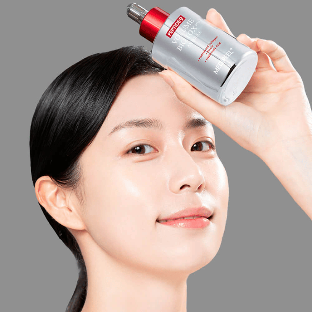 Une personne tient MEDI-PEEL Peptide 9 Volume Bio Tox Pro Ampoule contre son front. La peau semble hydratée et éclatante - le sérum renforce l'élasticité et la fermeté.