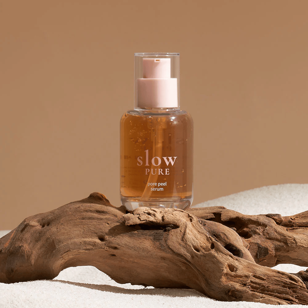 Slow Pure Pore Peel Serum placé sur du sable avec un détail en bois en arrière-plan, symbole de soins de la peau naturels.