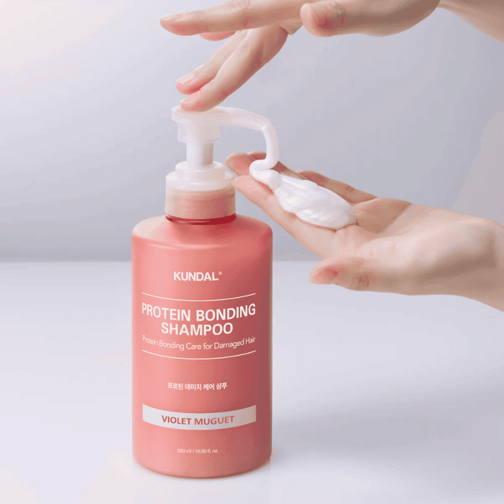 Une main pompe KUNDAL Protein Bonding Shampoo Violet Muguet à la consistance crémeuse, shampoing réparateur pour cheveux abîmés.