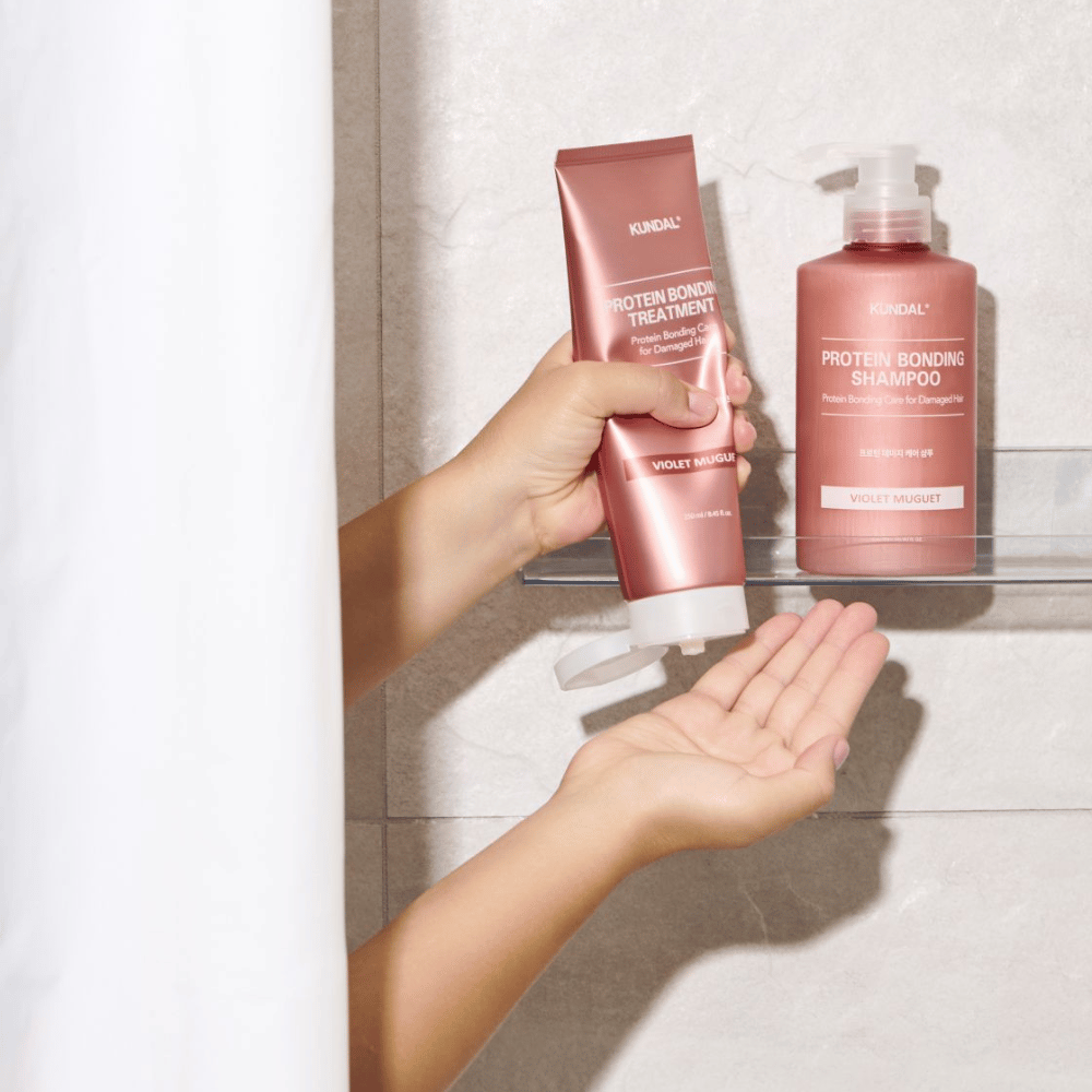 KUNDAL Liaison Protéique Treatment Violet Muguet utilisé sous la douche, avec Protein Bonding Shampoo placé sur l'étagère à côté.