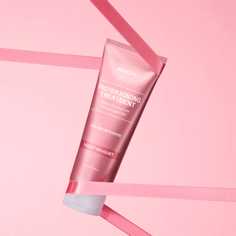 KUNDAL Protein Bonding Treatment Violet Muguet dans un tube rose de 250 ml sur fond rose avec des rubans décoratifs.